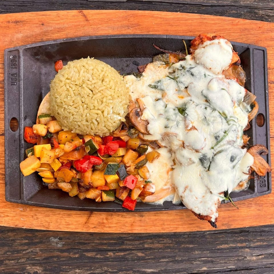 Melted cheese over a Mexican dish with rice and mixed vegetables on a black skillet.