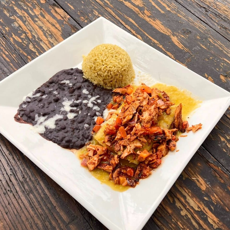 Mexican dish with rice, black beans, and shredded chicken in green sauce on a white plate.
