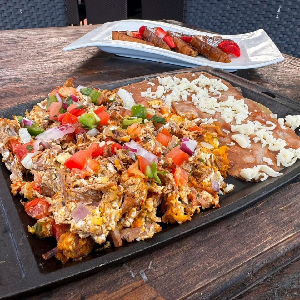 A sizzling platter of Mexican machaca con huevo with a cheese-covered tortilla, and French toast with strawberries.