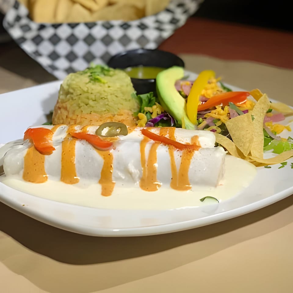 Mexican enchiladas with creamy sauce, rice, salad, avocado, and tortilla chips on a white plate.