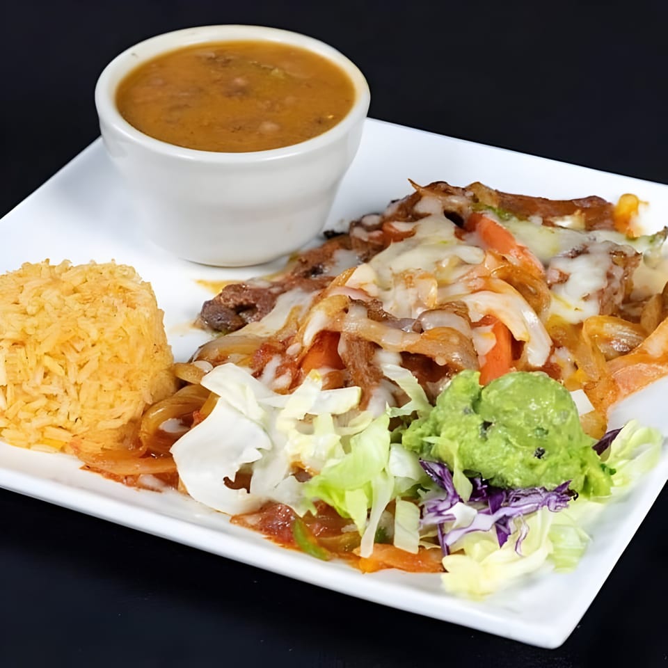 Mexican fajitas with melted cheese, rice, refried beans, guacamole, and salad on a white plate.