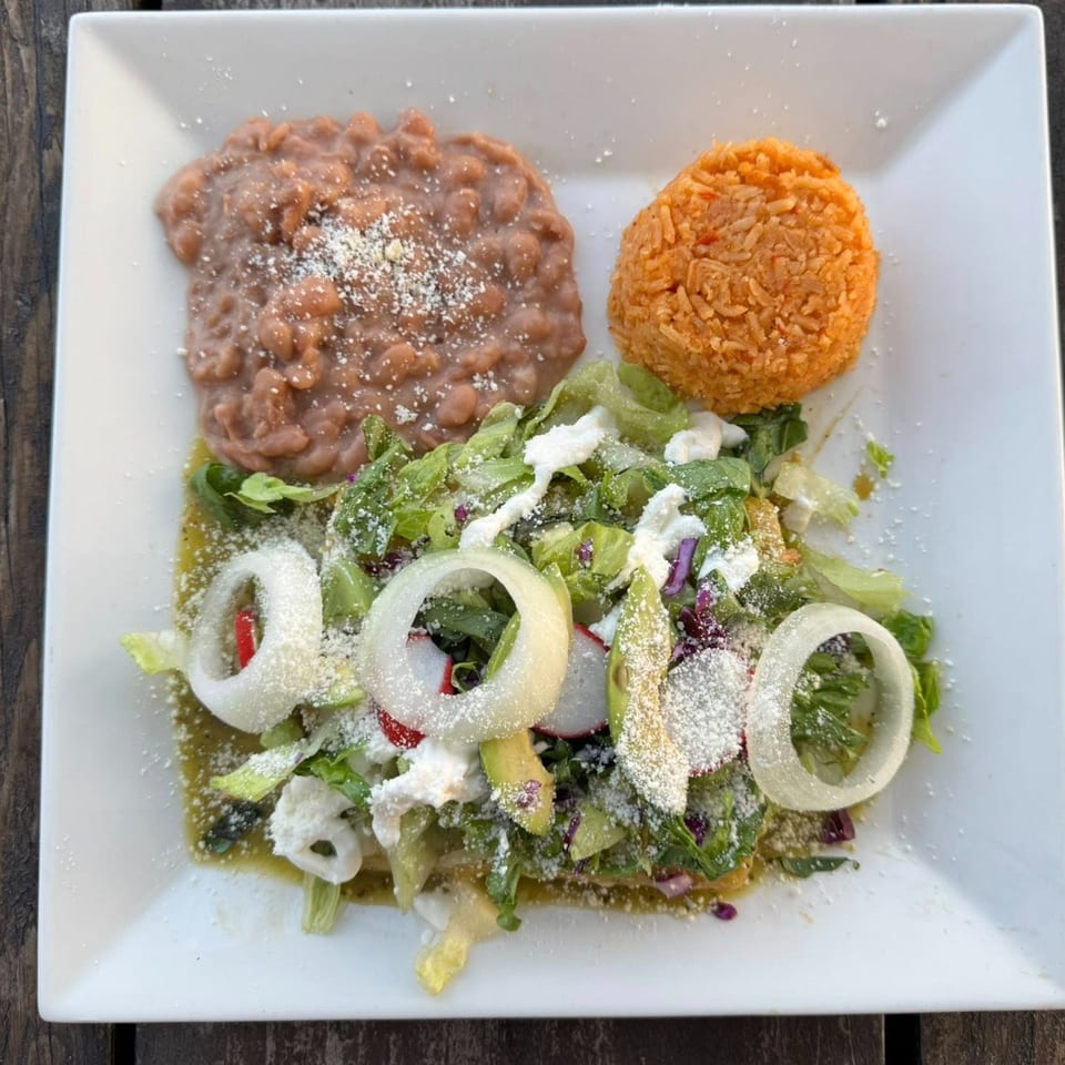 A Mexican dish with refried beans, orange rice, and a green salad with onions and cheese.