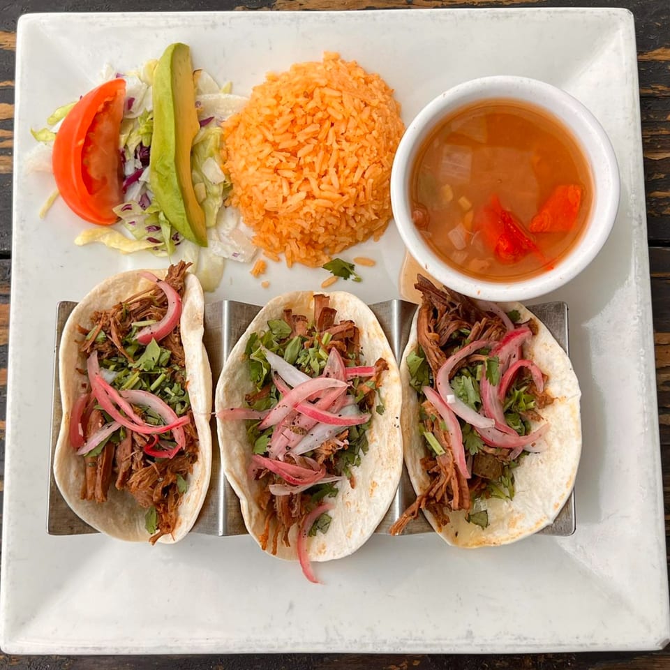 Three Mexican tacos with shredded meat, red onions, and cilantro, served with rice, salad, and soup.