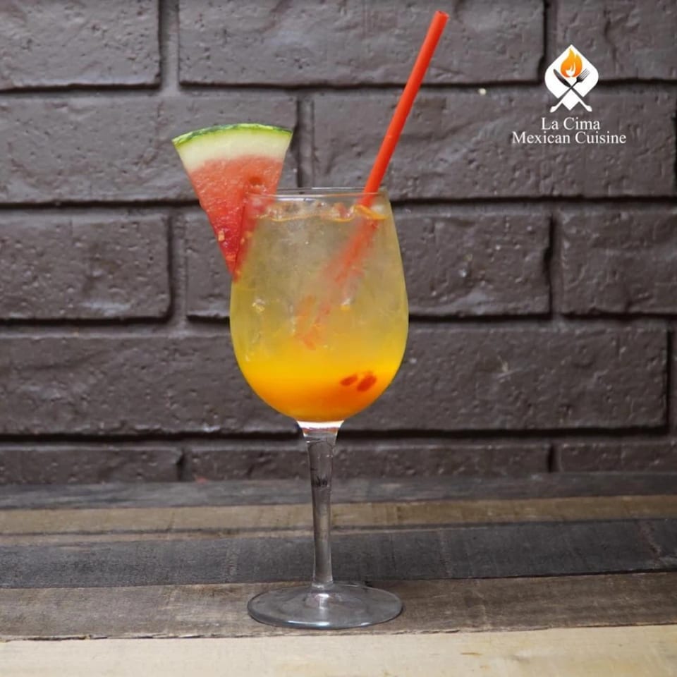 A refreshing La Cima Mexican Cuisine drink with a watermelon slice and red straw.